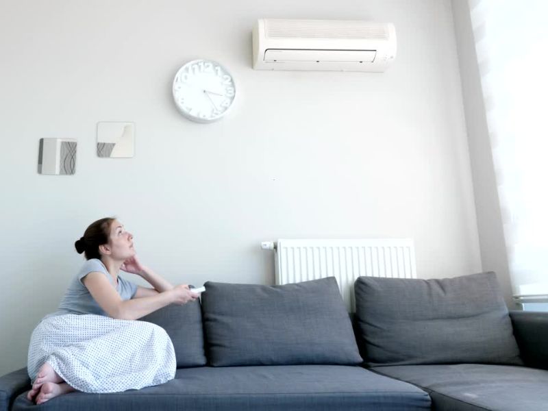 devojka sedi na ugaonoj i podešava inverter klimu